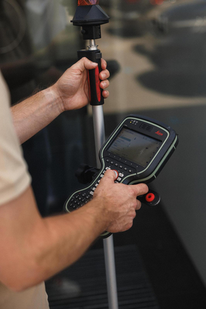 Landmeter met een meetstok met prisma en een Leica veldcomputer
