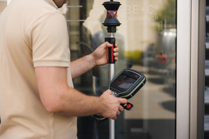 Landmeter met een meetstok met prisma en een Leica veldcomputer aan het kantoor