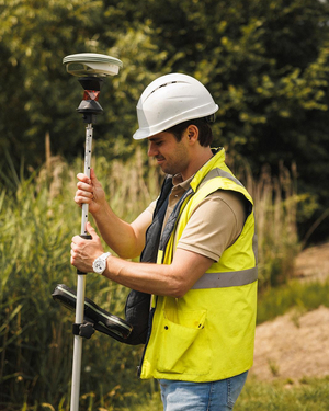 Landmeter met helm en fluohesje meet een punt op met een GNSS-meetstok